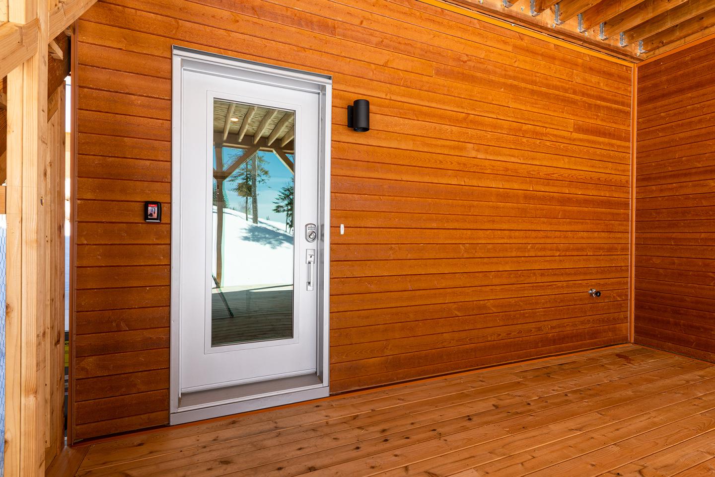 Porte en verre encadrée de bois, plafond et murs en bois clair.