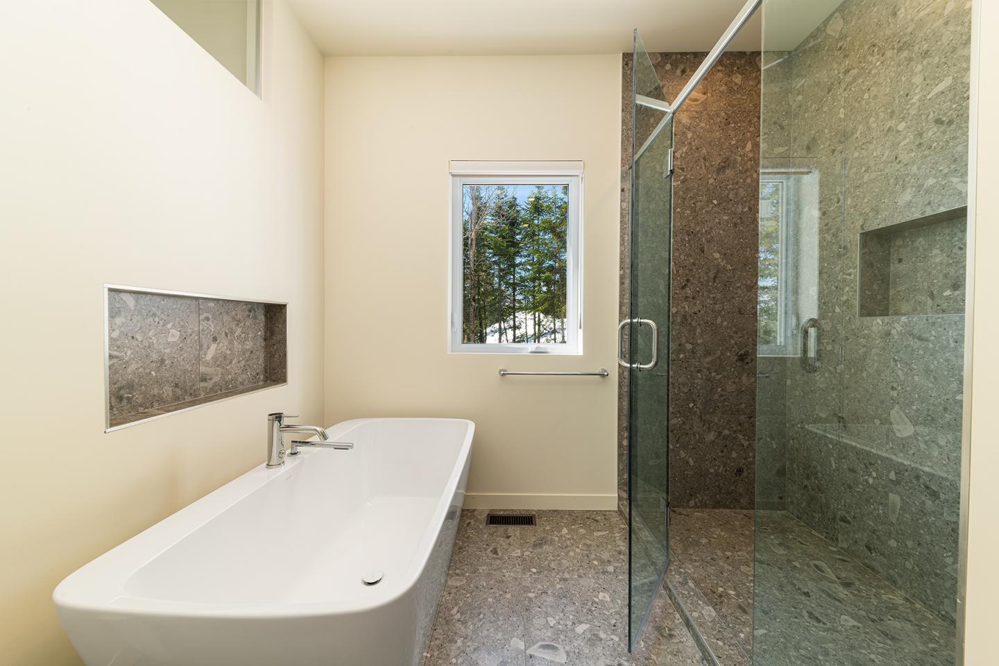 Salle de bain moderne avec baignoire, douche en verre et fenêtre extérieure.