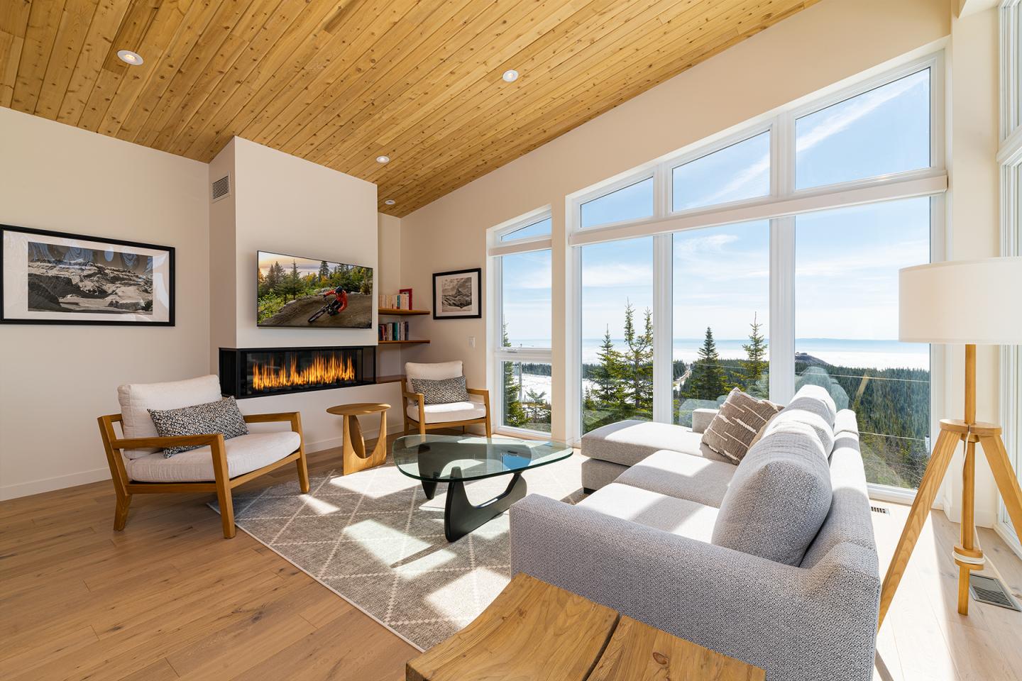 Salon moderne avec vue sur montagne, grandes fenêtres, cheminée et mobilier confortable.