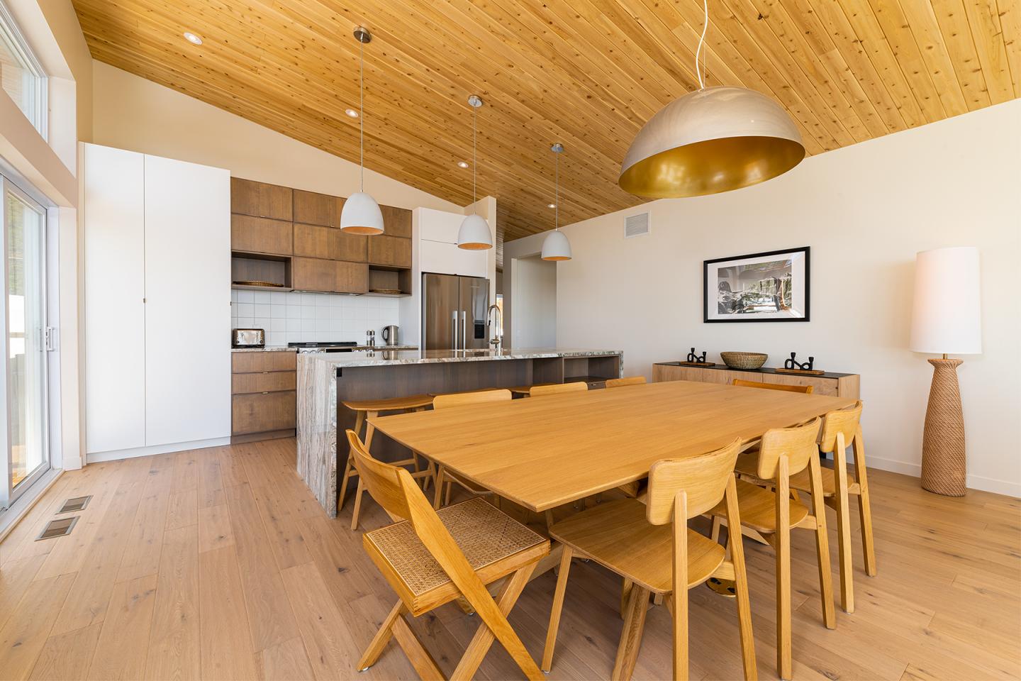 Salle à manger moderne en bois clair, table et chaises, cuisine ouverte au fond.