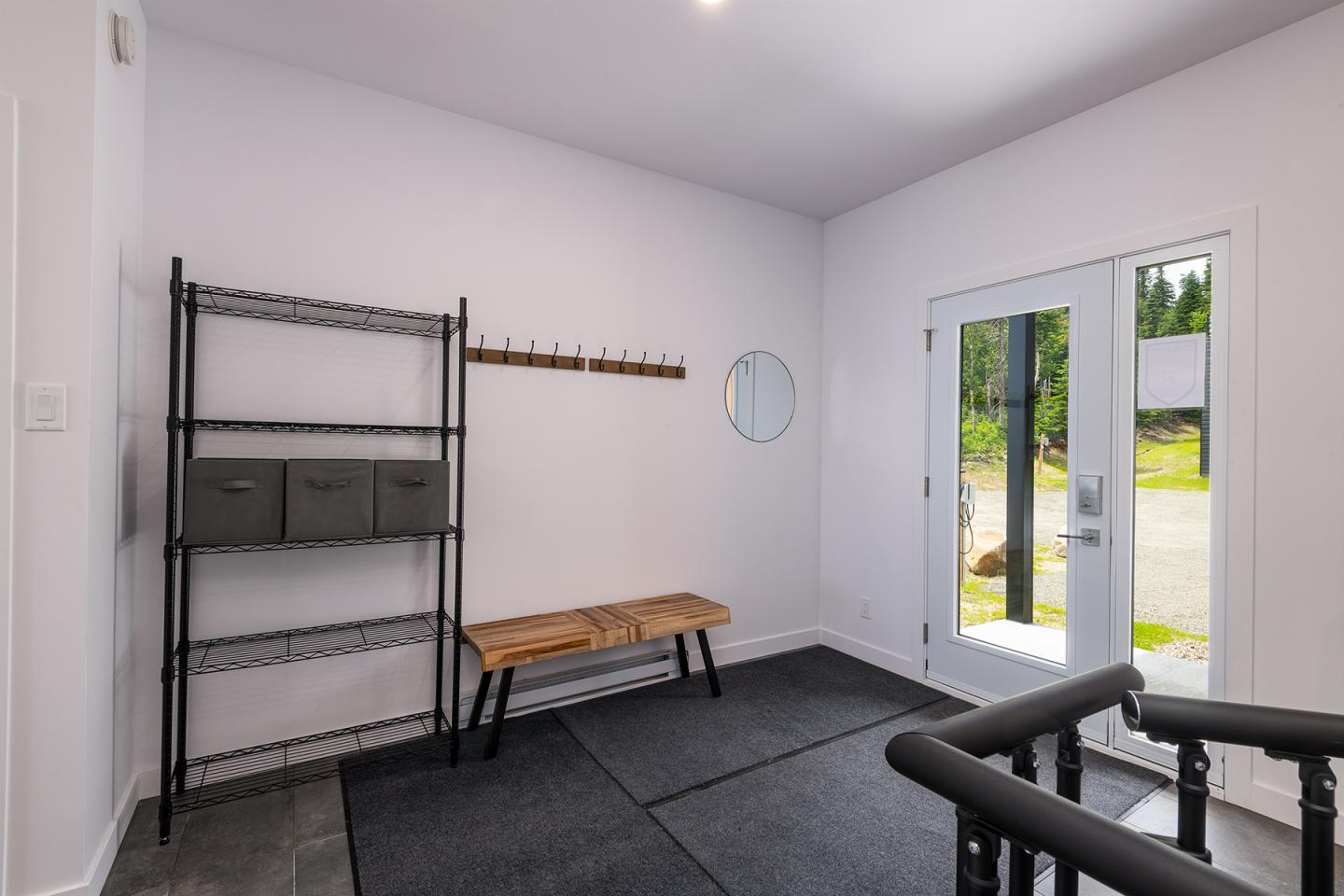 Vestibule lumineux avec banc en bois, étagère noire et porte-fenêtre donnant sur jardin.