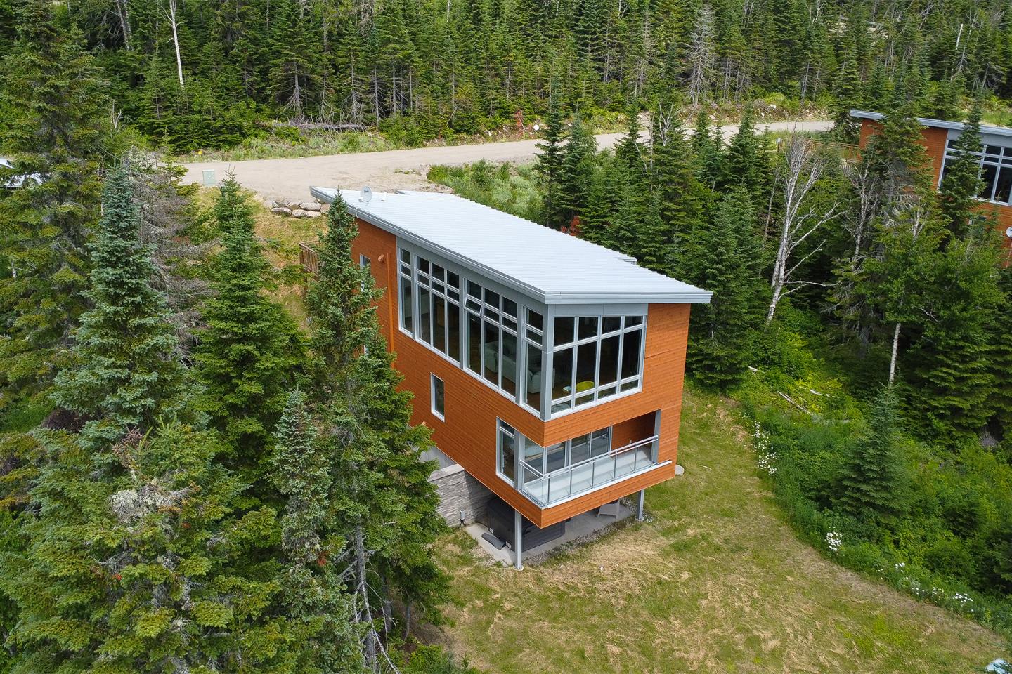 Maison moderne en bois orange entourée de forêt verdoyante.