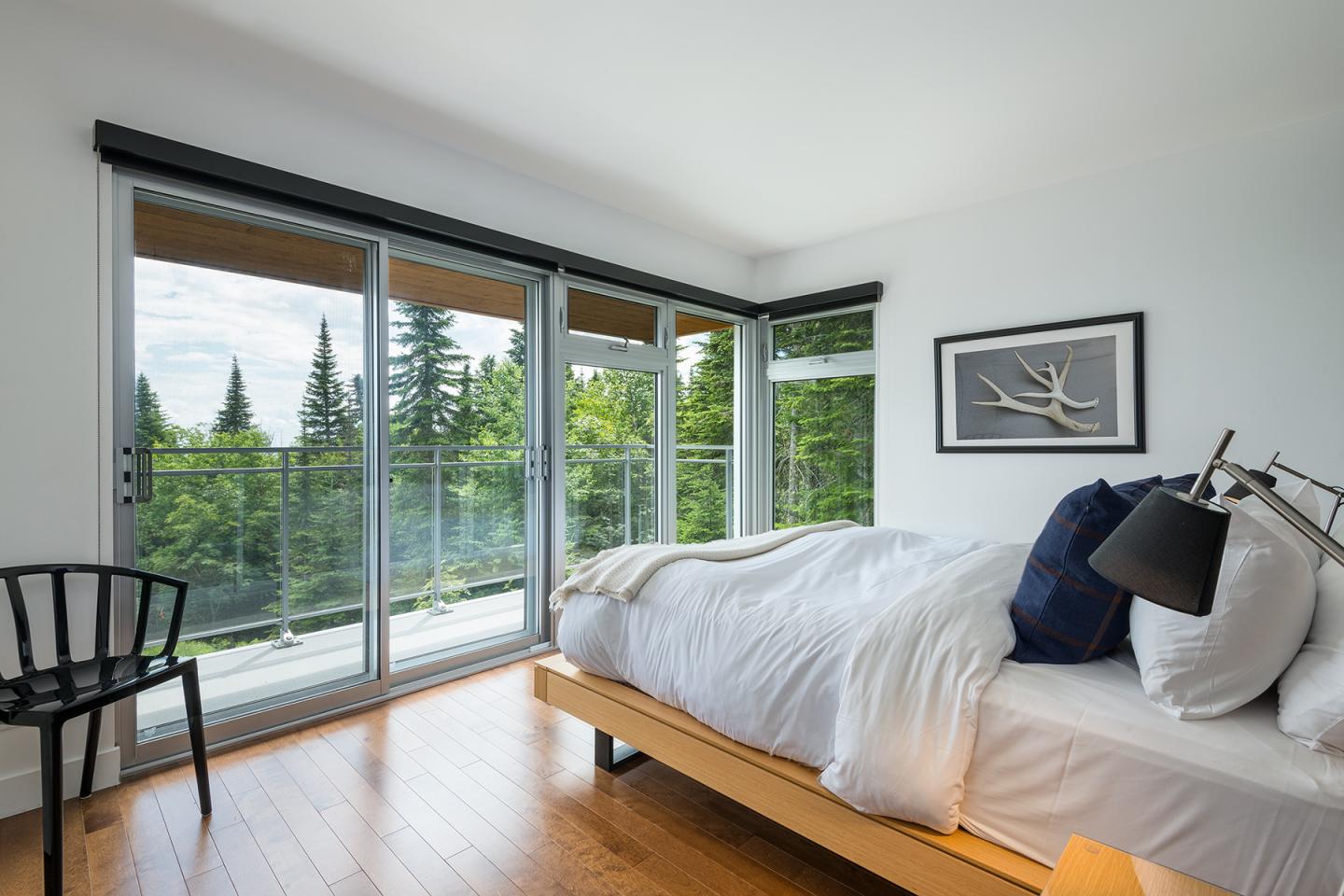 Chambre lumineuse avec lit blanc, baie vitrée donnant sur la forêt.