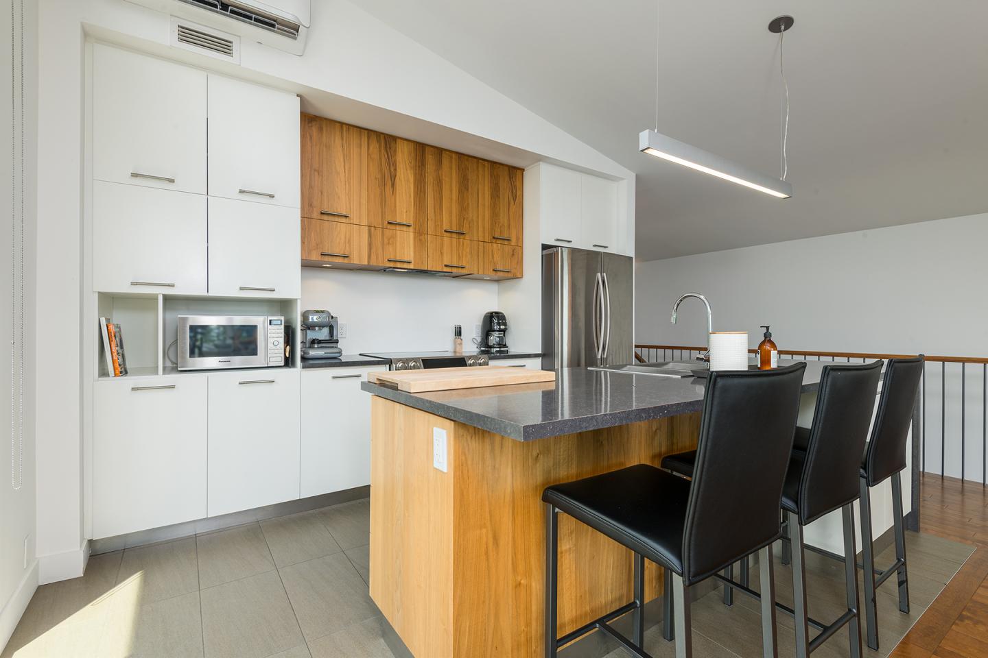 Cuisine moderne avec îlot central, chaises noires, électroménagers en acier inoxydable.
