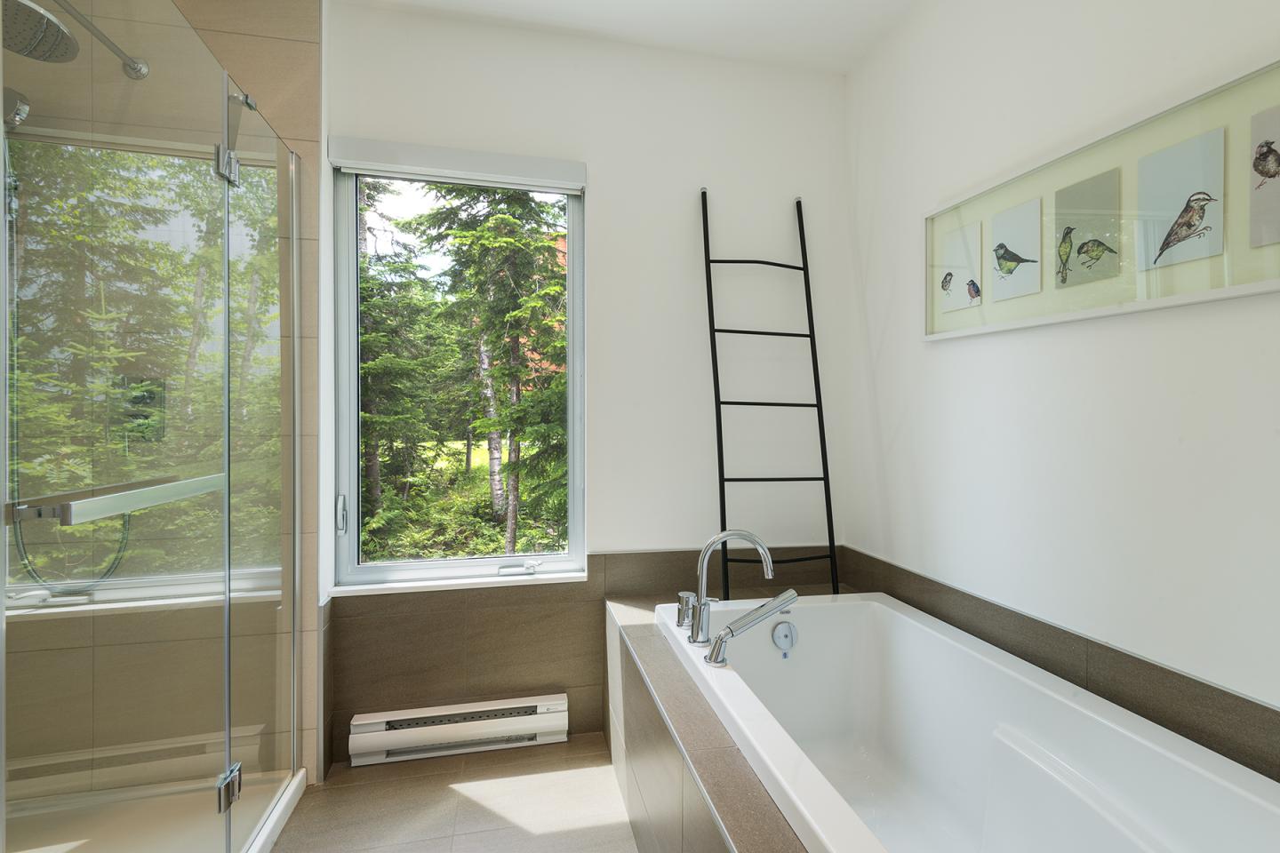 Salle de bain moderne avec baignoire, douche vitrée et vue sur la forêt.