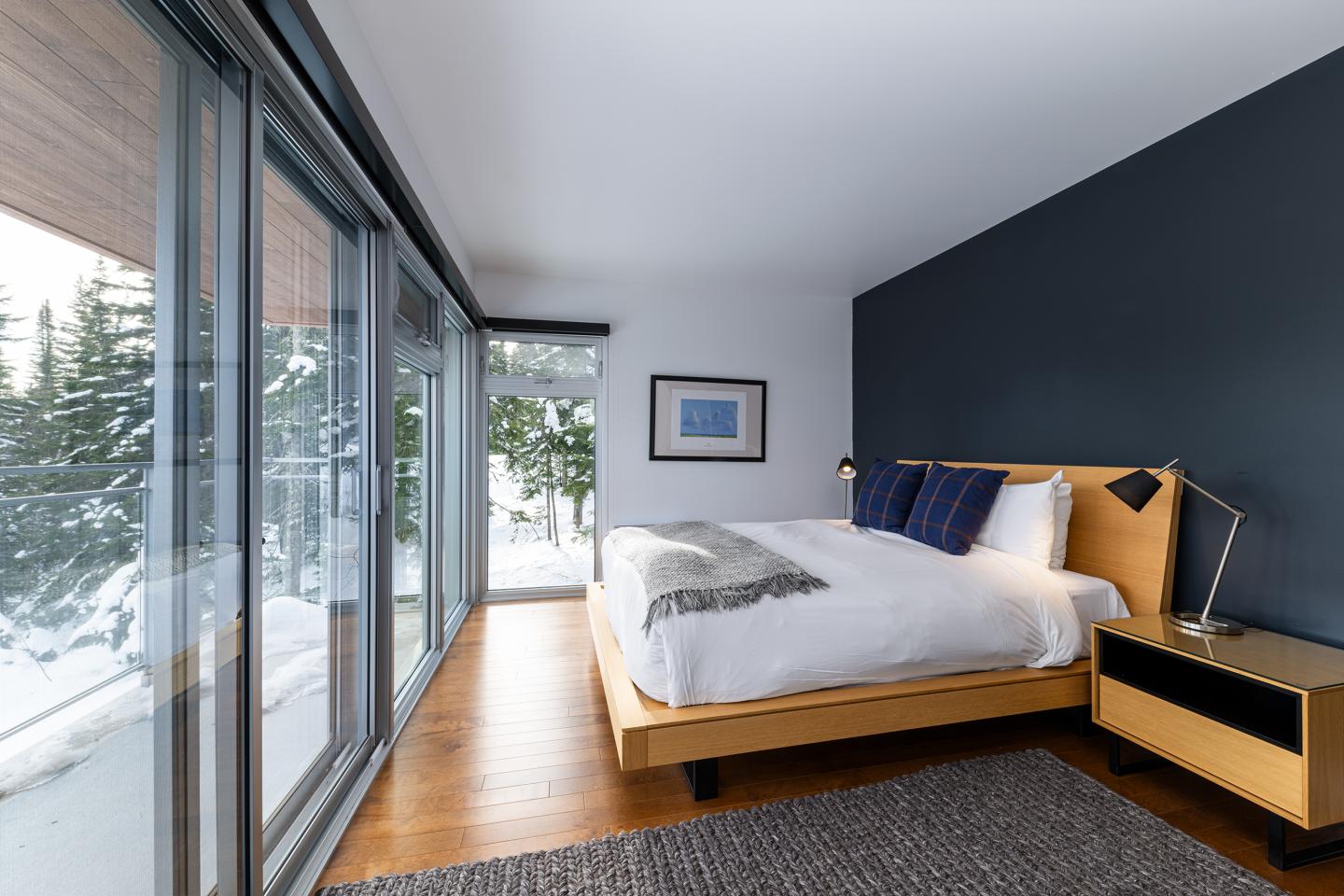 Chambre moderne avec lit double près d'une baie vitrée donnant sur des arbres enneigés.