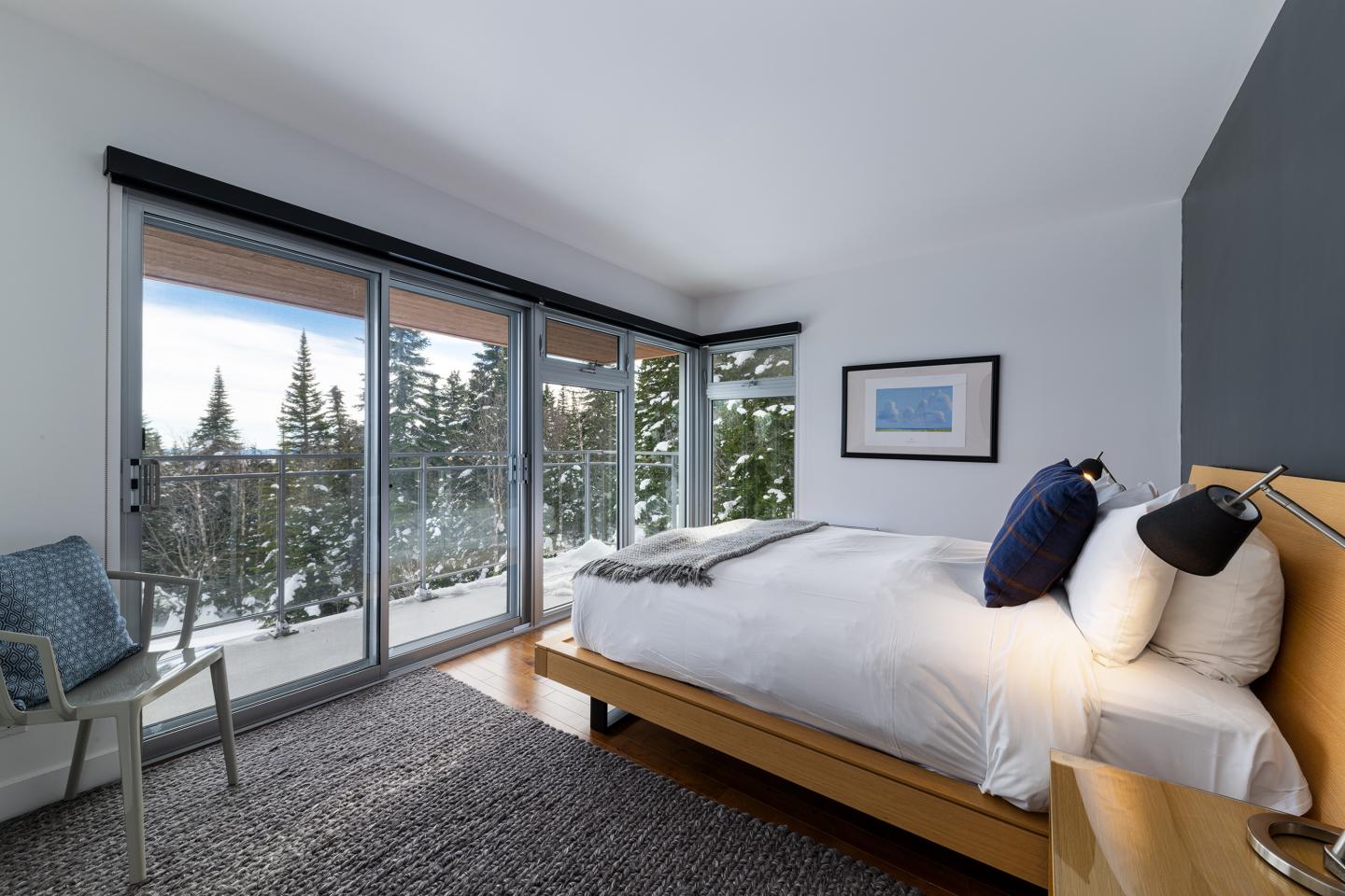 Chambre moderne avec un grand lit et vue sur la forêt enneigée.