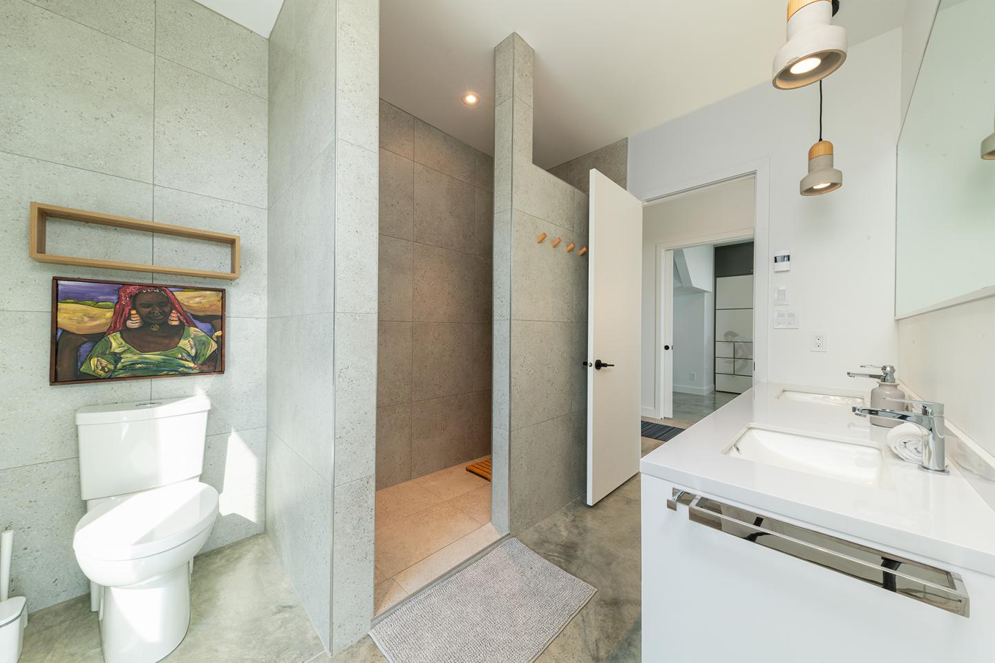 Salle de bain moderne avec douche ouverte, lavabo blanc, et éclairage suspendu.