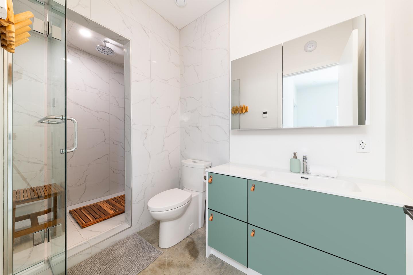 Salle de bain moderne avec douche vitrée, lavabo turquoise et miroir.