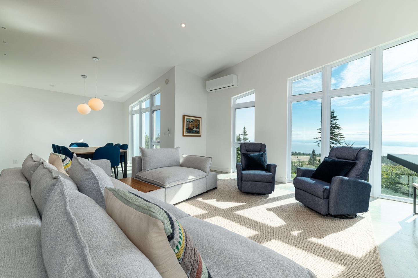 Salon lumineux avec grands canapés, fauteuils, et vue sur l'océan à travers des baies vitrées.