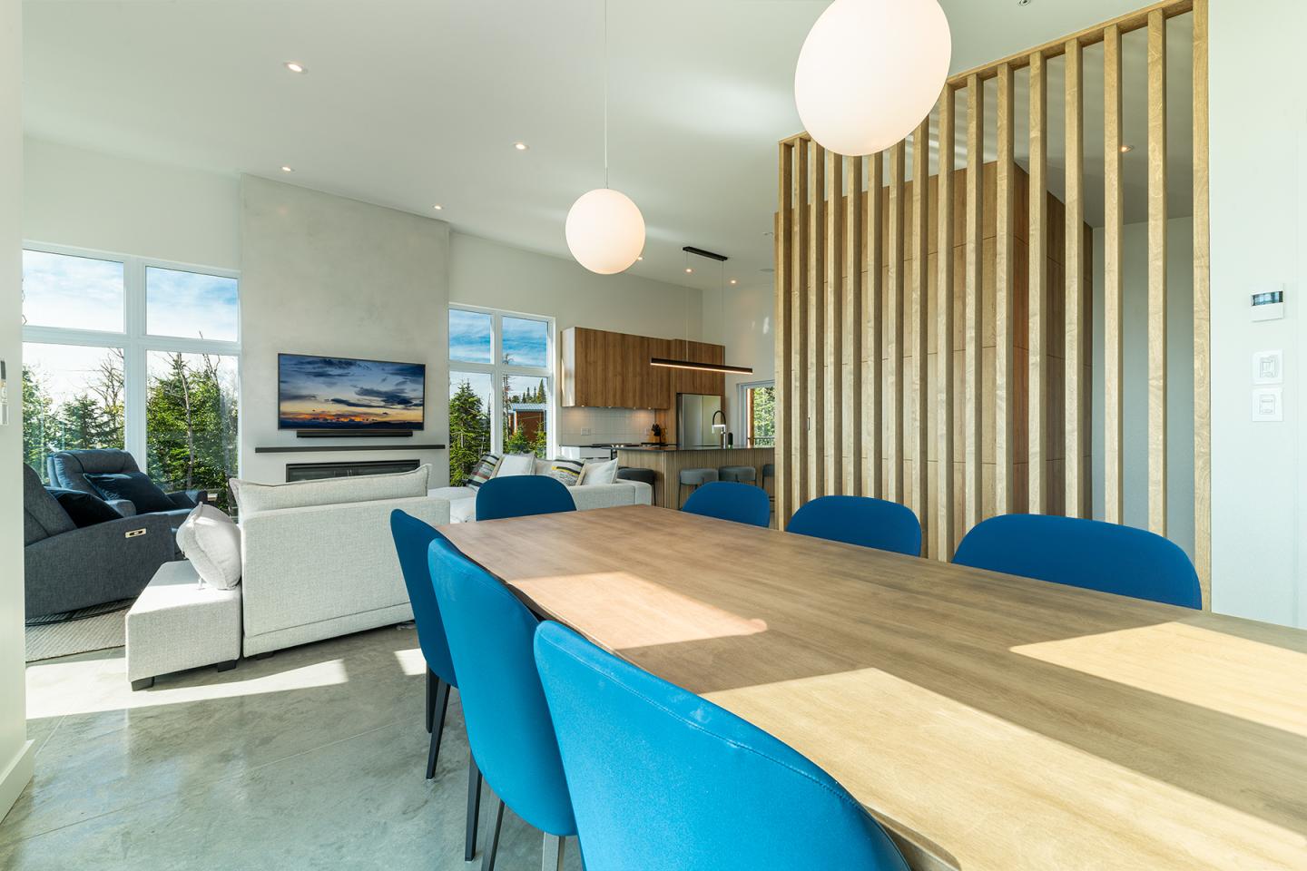 Salle à manger moderne avec table en bois, chaises bleues et luminaires sphériques.
