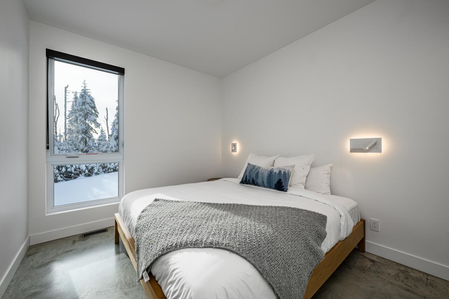 Chambre moderne blanche avec lit double, fenêtre avec vue sur arbres enneigés.