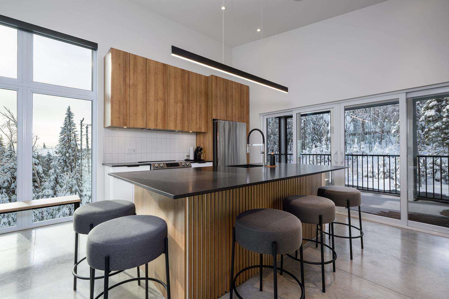 Cuisine moderne avec îlot central et tabourets, grandes fenêtres sur paysage enneigé.