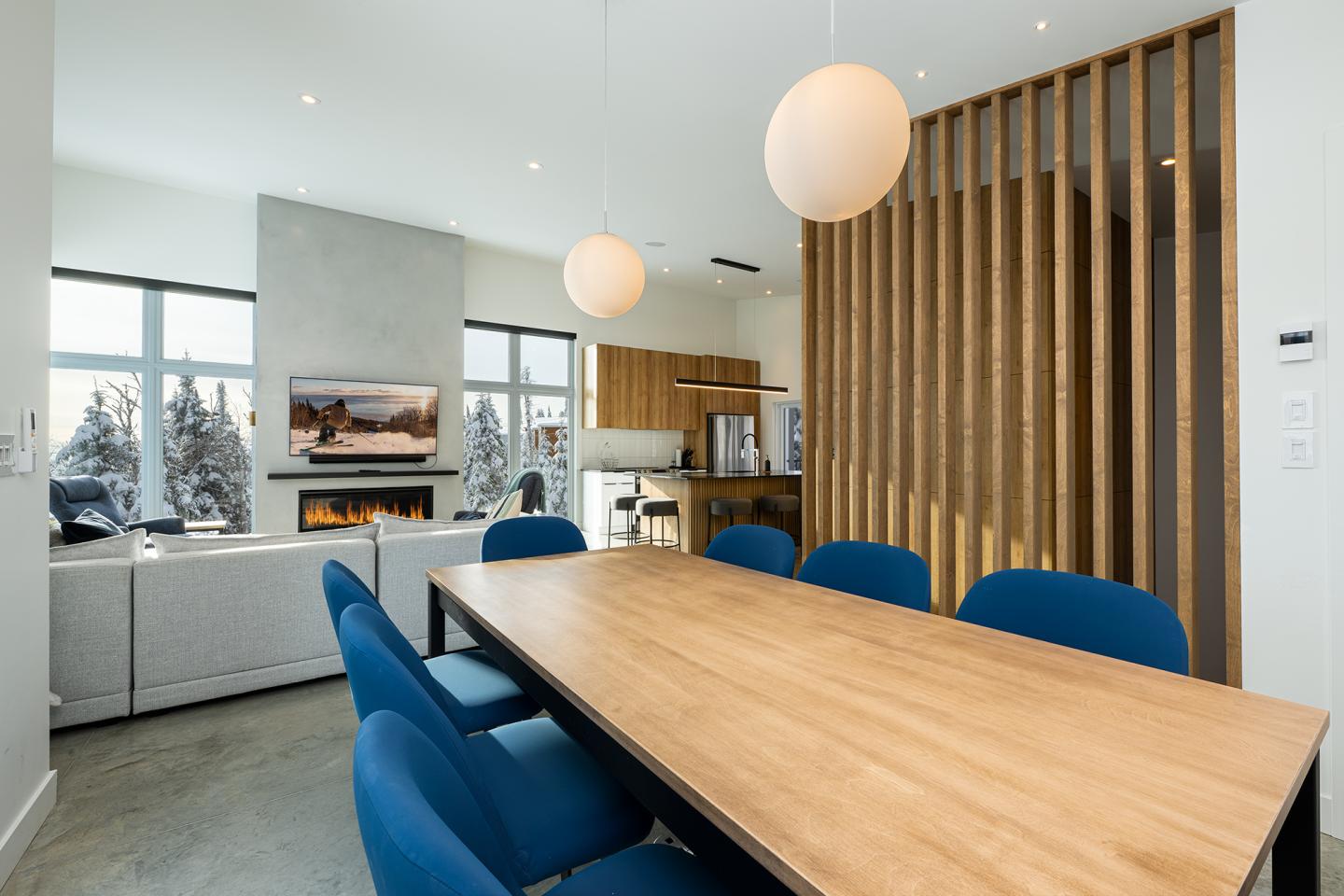 Salle à manger moderne avec table en bois et chaises bleues, lampes suspendues.
