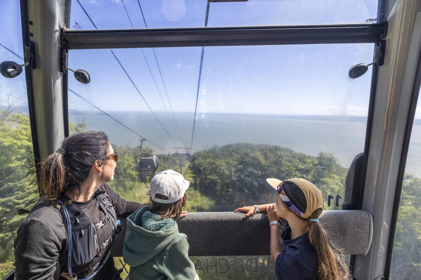 Famille admirant la vue depuis une cabine de téléphérique au-dessus de la mer.