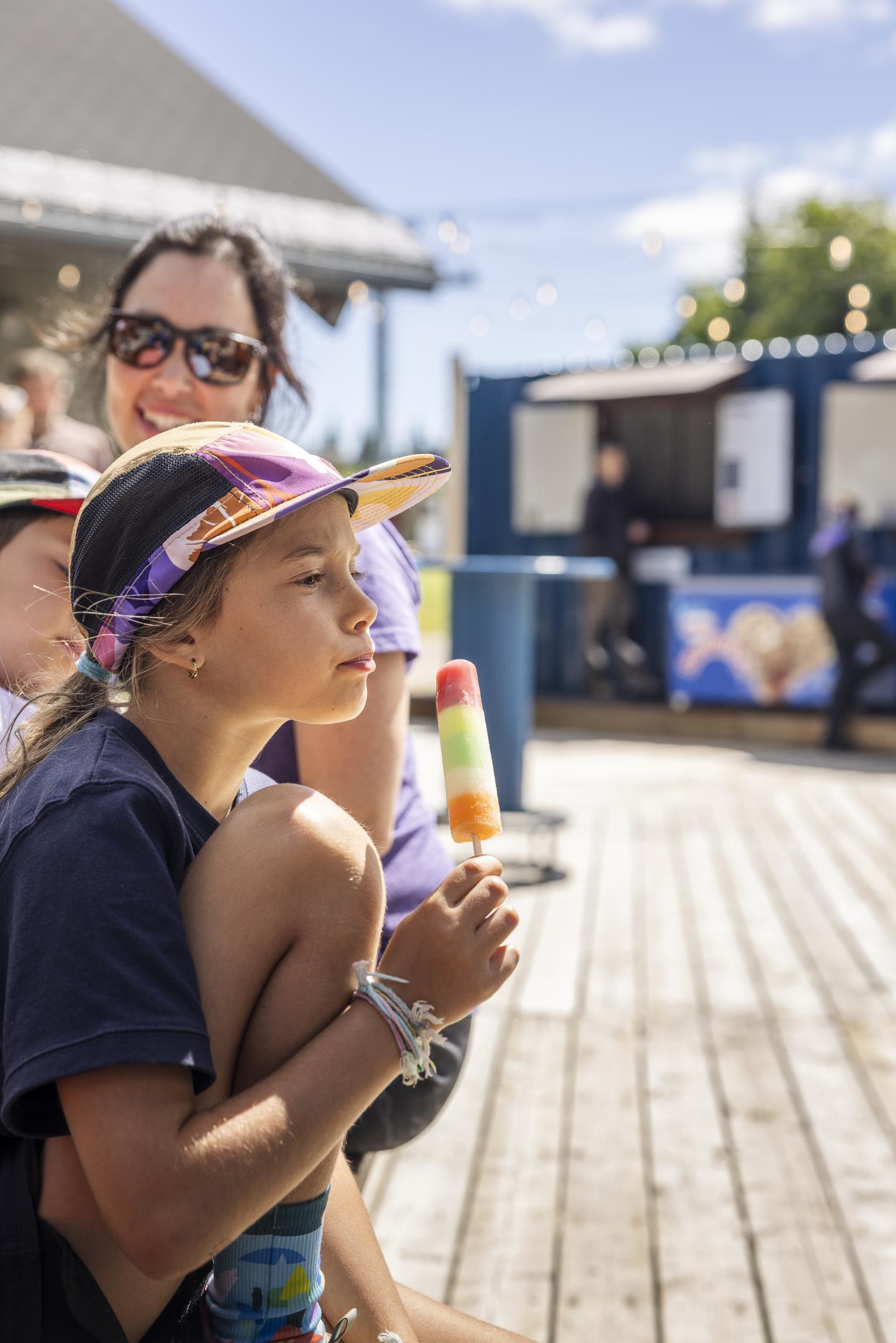 Enfant avec une glace, assise par terre, extérieur ensoleillé.