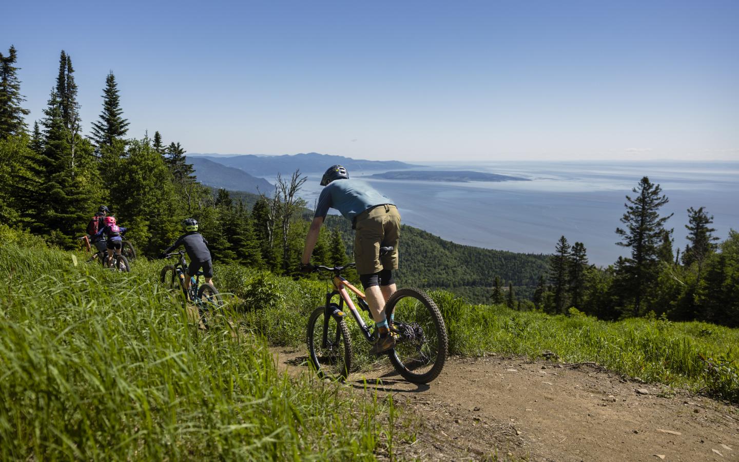 Cyclistes descendant un sentier de montagne, vue sur la mer et forêt.