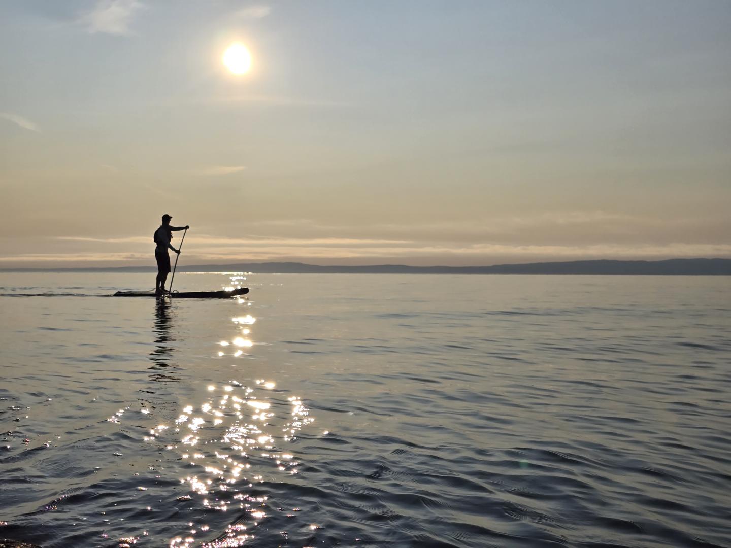 Planche à pagaie sur un lac au coucher du soleil.