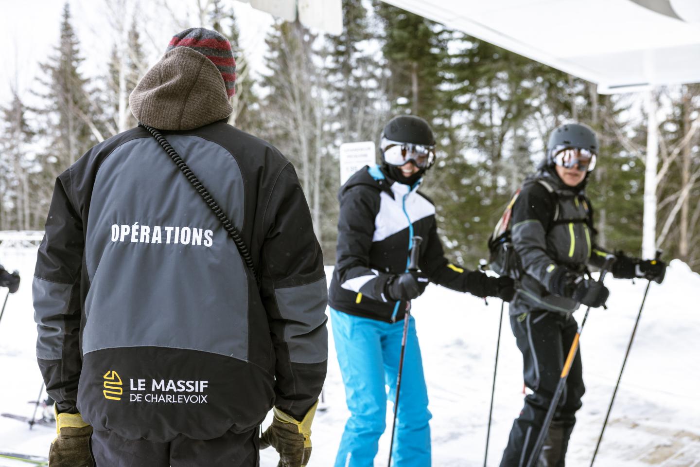 Personne avec manteau "Opérations" devant skieurs souriants en hiver.