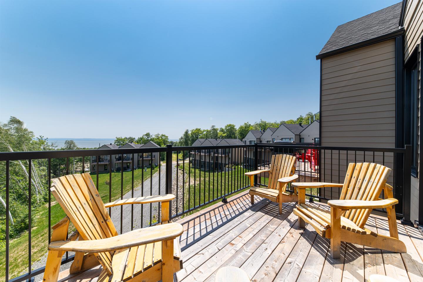 Terrasse en bois avec chaises Adirondack, vue sur jardin et maisons.