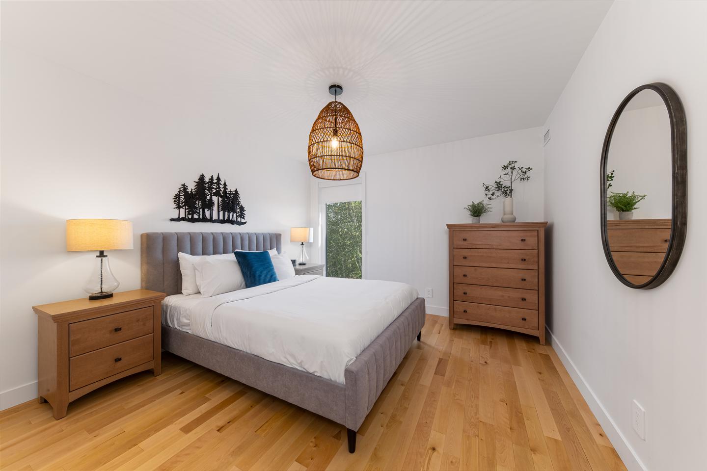 Chambre lumineuse avec lit double, commode, et miroir ovale.