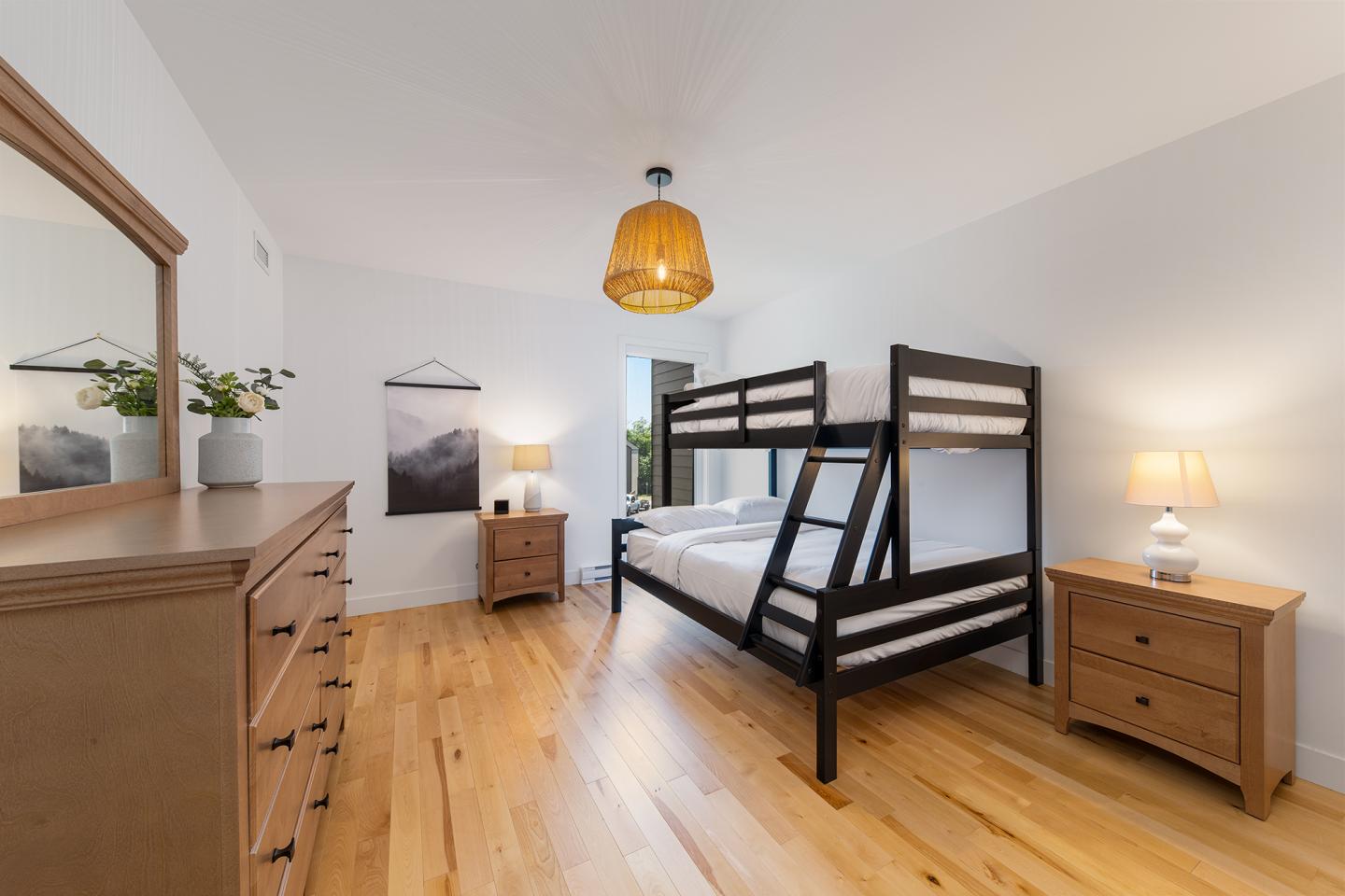 Chambre claire avec lit superposé, commodes en bois, et lampe suspendue.
