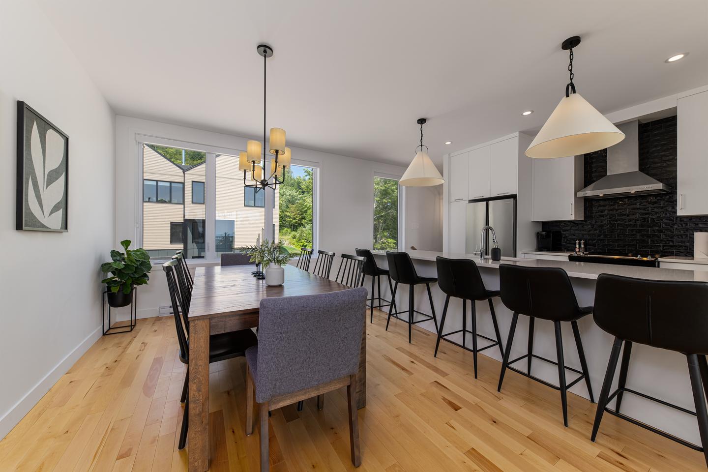 Salle à manger moderne avec table en bois, chaises noires et lumière naturelle.