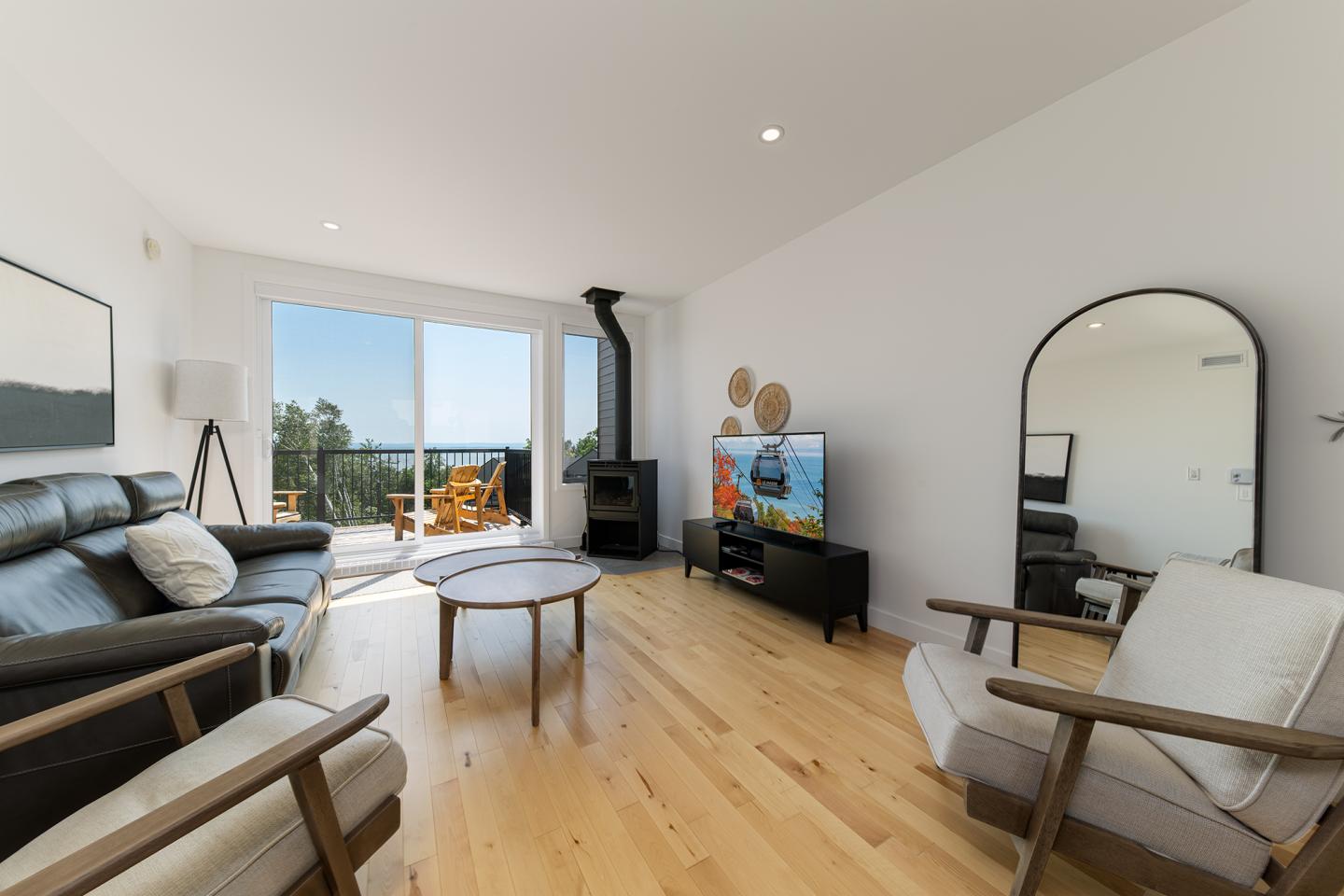 Salon moderne avec canapé, fauteuils, télévision et vue sur terrasse extérieure.