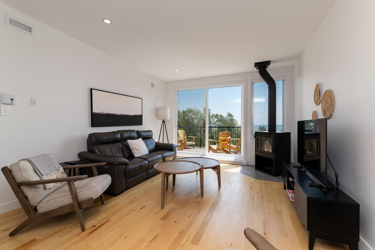 Salon moderne avec canapé, fauteuils, poêle à bois et grande baie vitrée vue sur jardin.