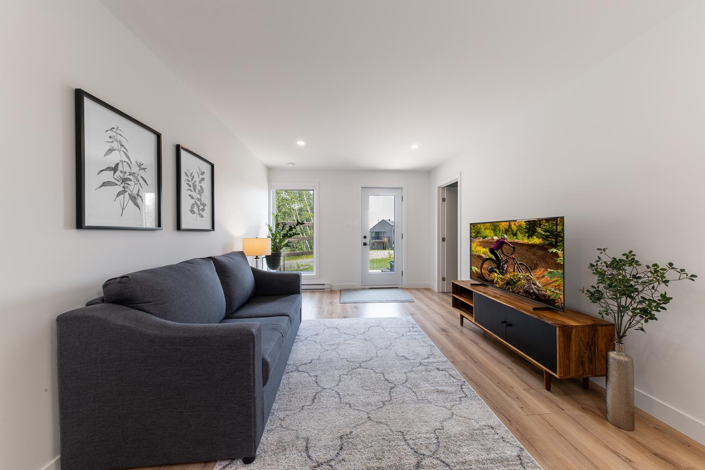 Salon moderne avec canapé gris, télé sur meuble en bois, et décorations minimalistes.