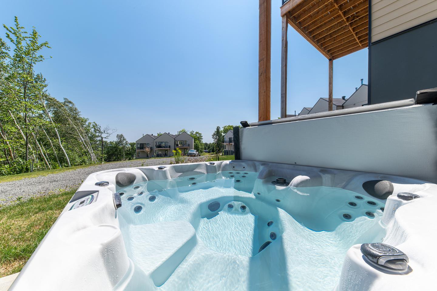 Jacuzzi extérieur avec eau claire, entouré de verdure et maisons au loin.