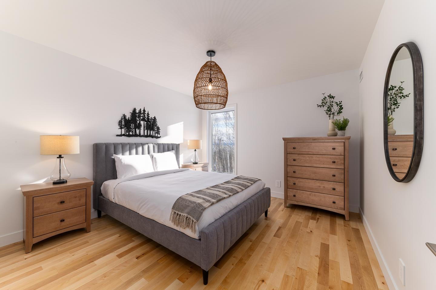Chambre moderne avec lit double, lampe suspendue, commode en bois et miroir ovale.