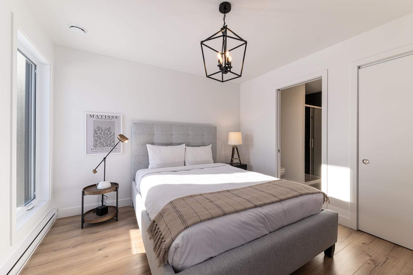 Chambre lumineuse avec lit double, lampe de bureau, parquet et déco minimaliste.