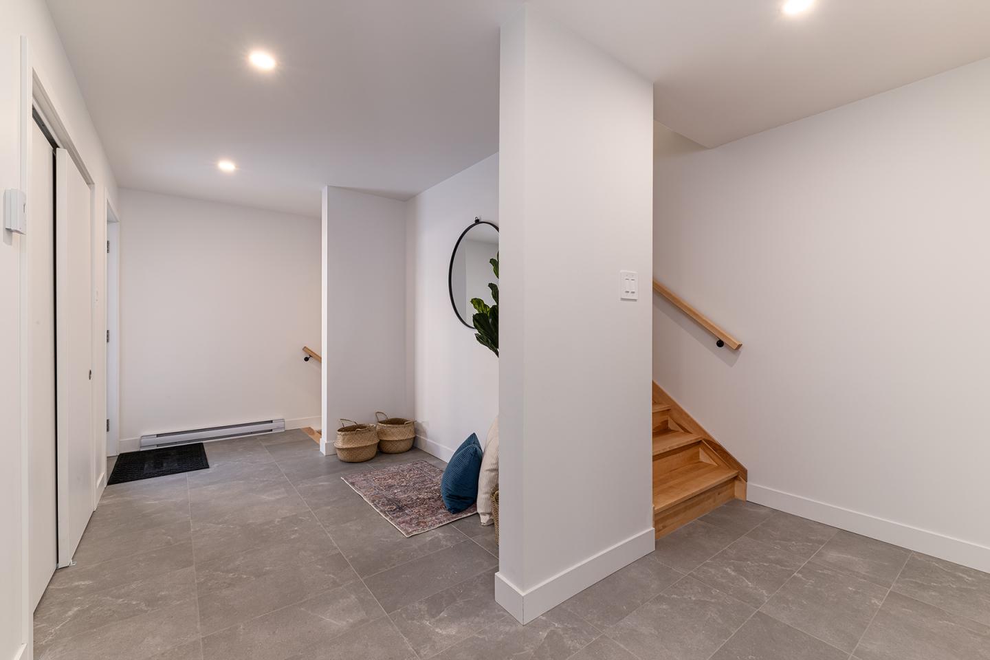 Entrée moderne avec carrelage gris, escalier en bois et miroir rond.