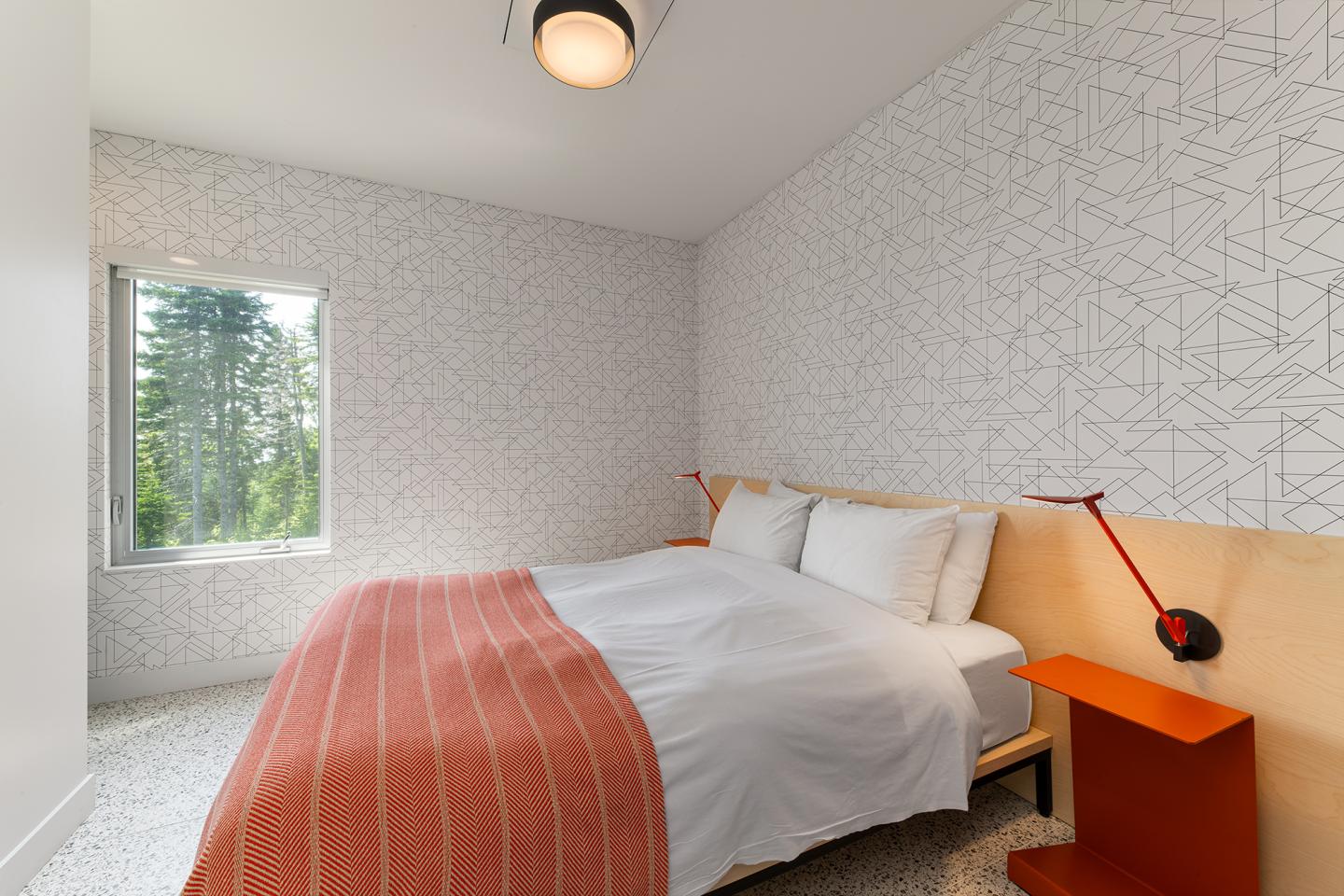 Chambre moderne avec lit double, lampe rouge, fenêtre avec vue sur la forêt.