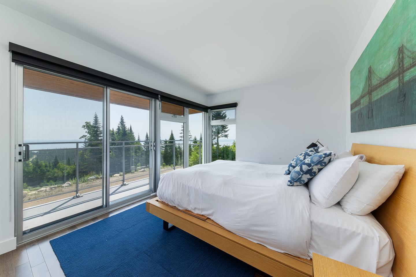 Chambre moderne avec lit double, grandes fenêtres, vue sur la terrasse et la forêt.