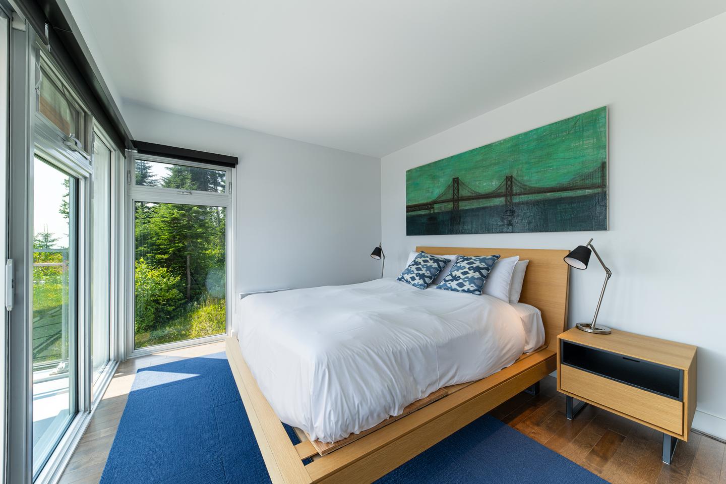 Chambre lumineuse avec lit double, grand tableau et baie vitrée.
