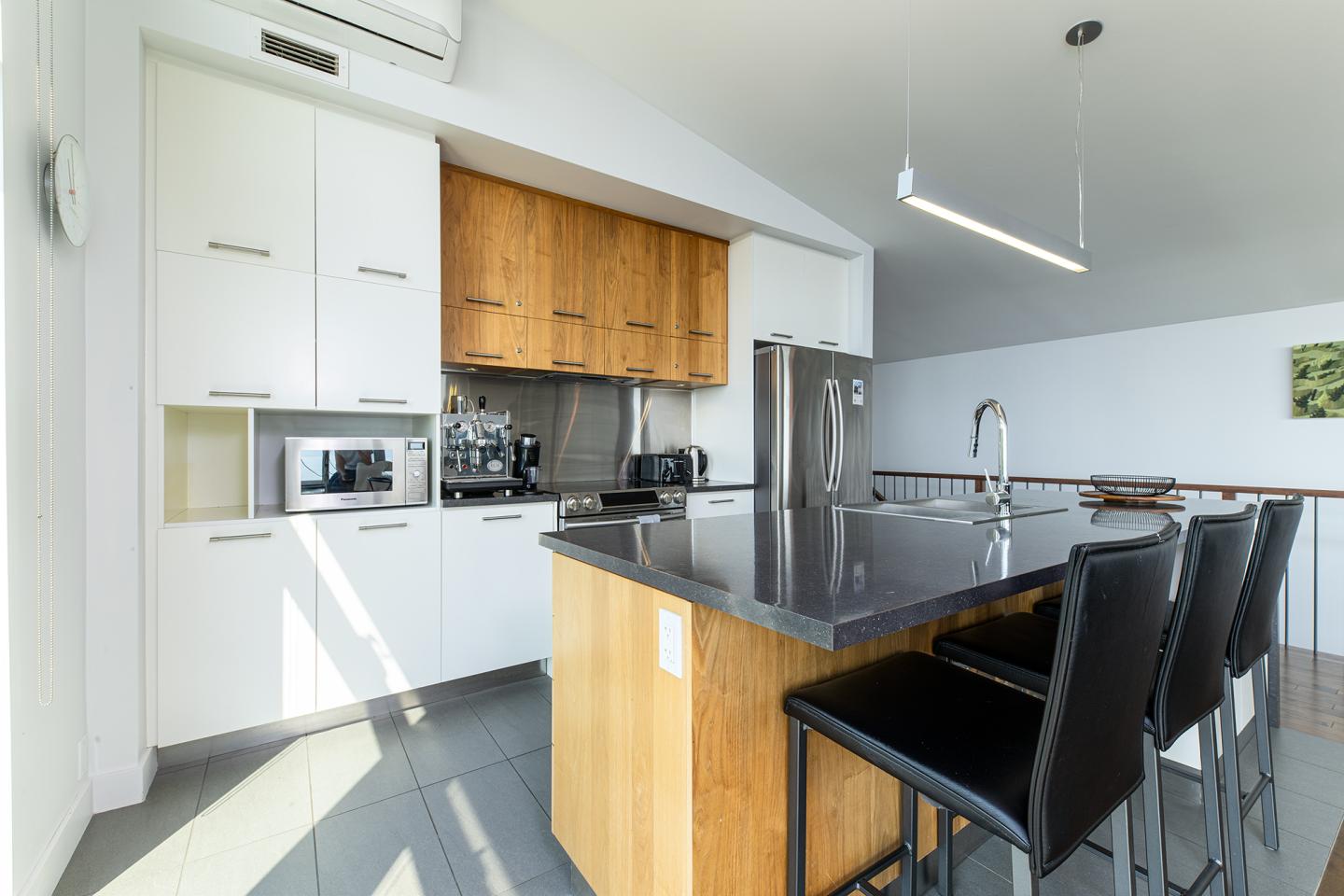 Cuisine moderne avec îlot central, tabourets noirs et plan de travail gris.