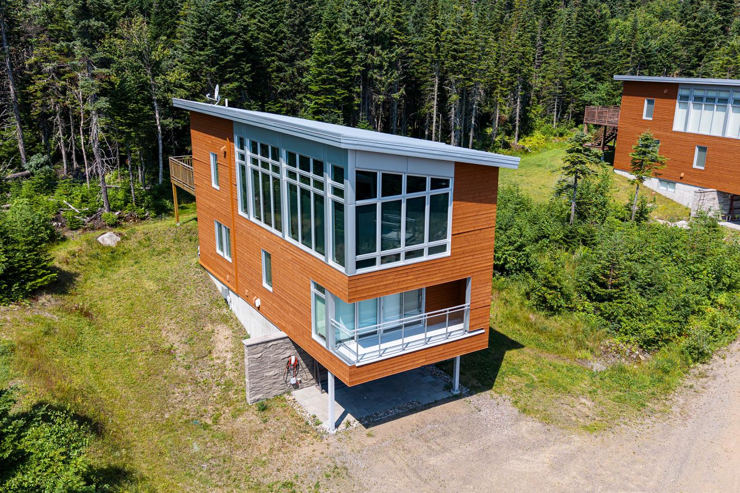 Maison moderne en bois, grandes fenêtres, bordée de forêt.