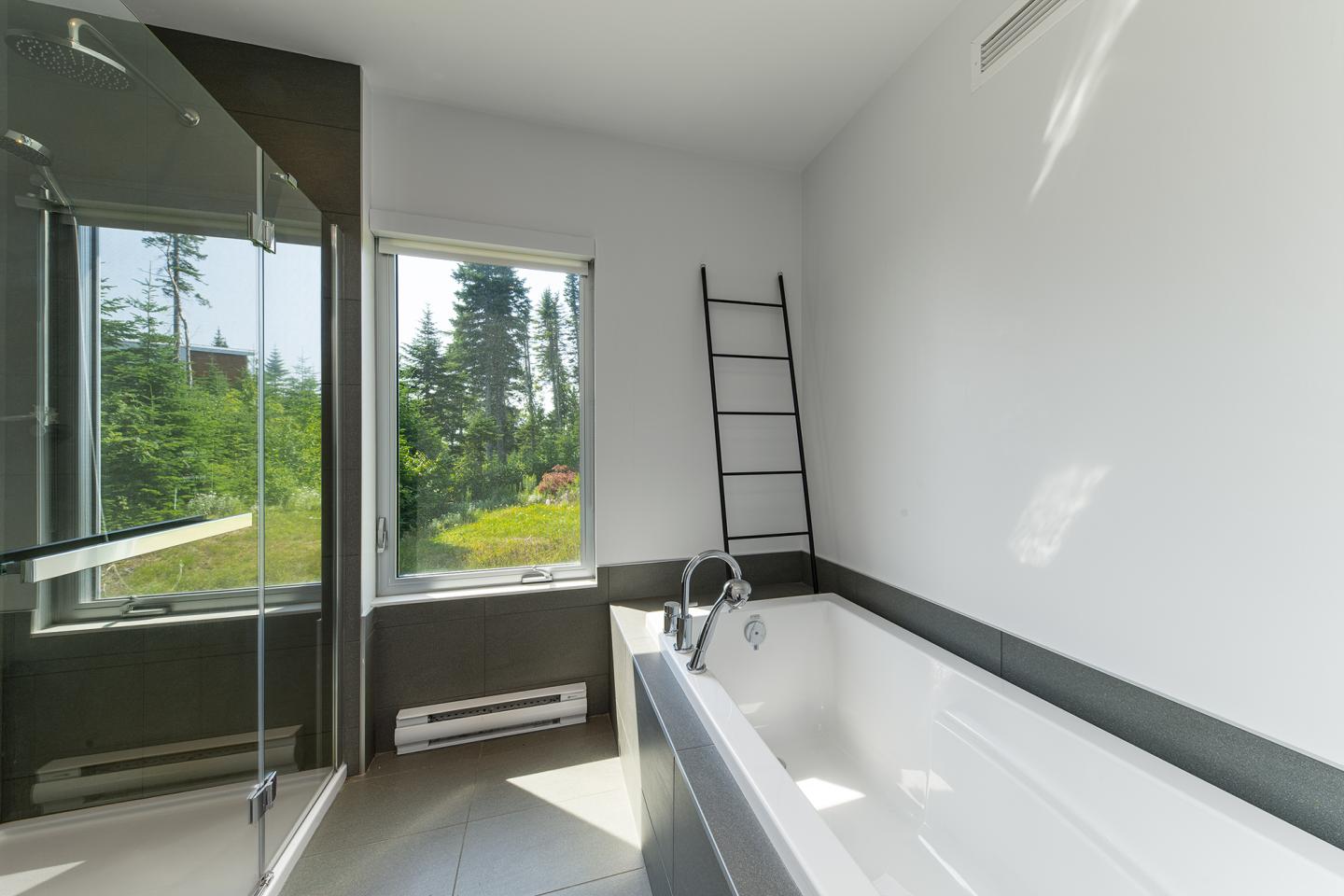 Salle de bain moderne avec baignoire, fenêtre sur verdure, et échelle murale noire.