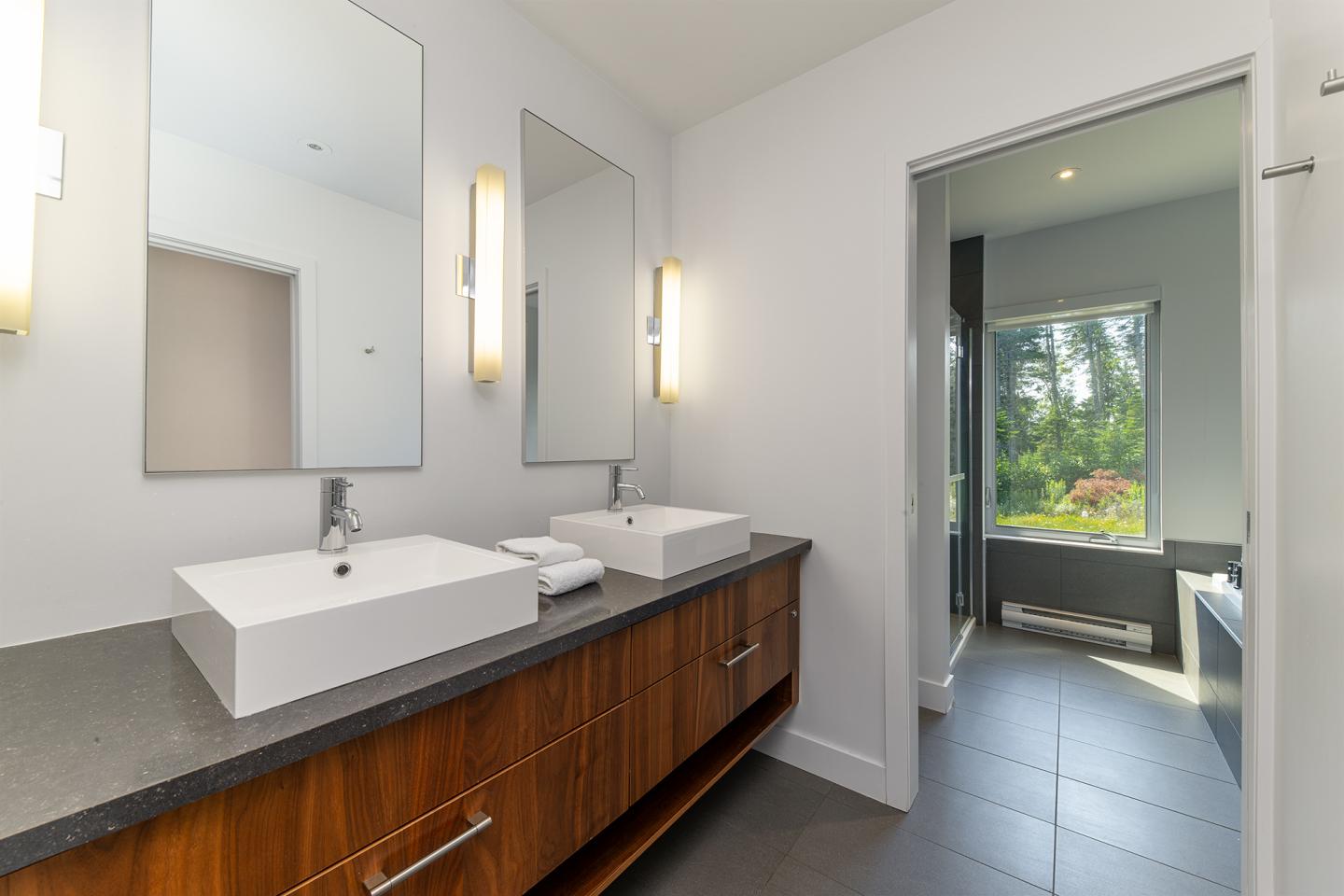 Salle de bain moderne avec deux lavabos, miroirs et vue sur jardin.