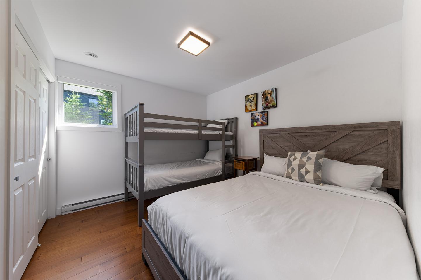 Chambre lumineuse avec lit double et lits superposés, murs blancs et parquet.