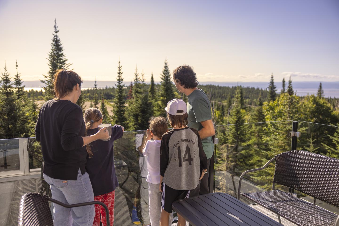 Famille contemplant une vue forestière depuis une terrasse, ciel dégagé.