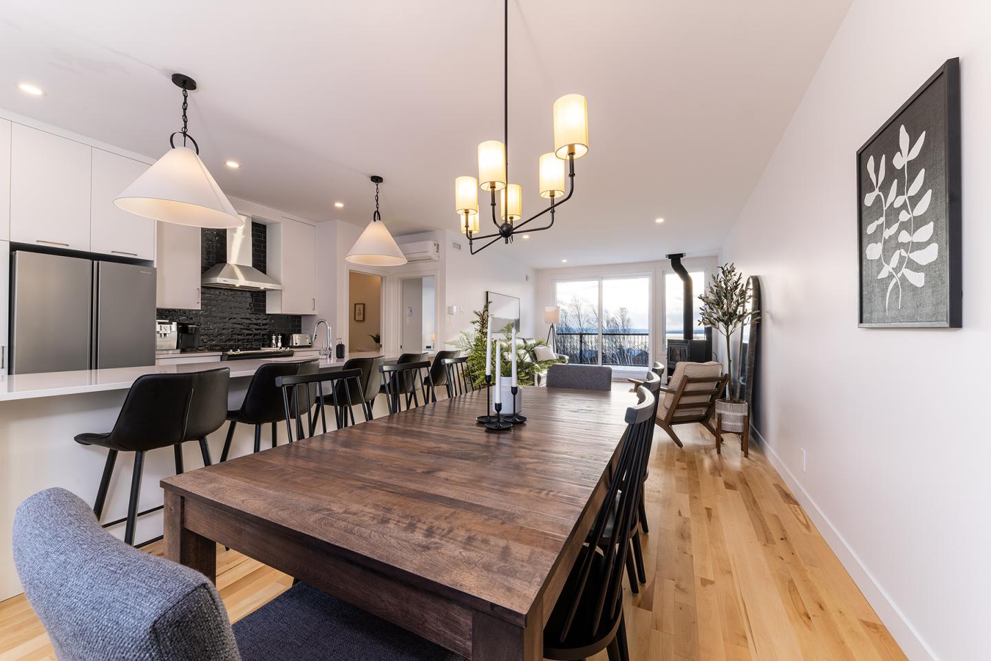 Salle à manger moderne avec table en bois, chaises noires et suspension élégante.