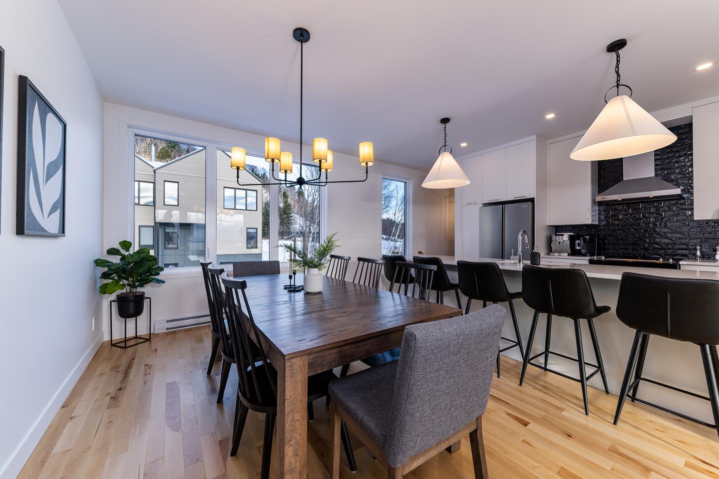 Salle à manger moderne avec grande table en bois, chaises noires et suspensions élégantes.