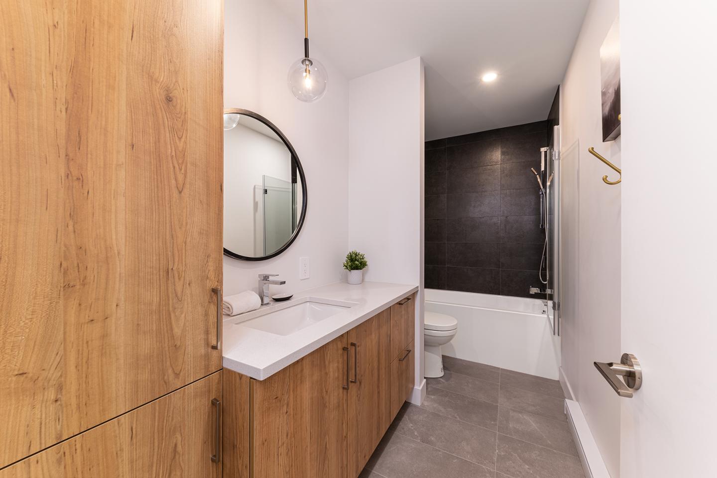 Salle de bain moderne avec mur sombre, meuble en bois, et miroir rond.