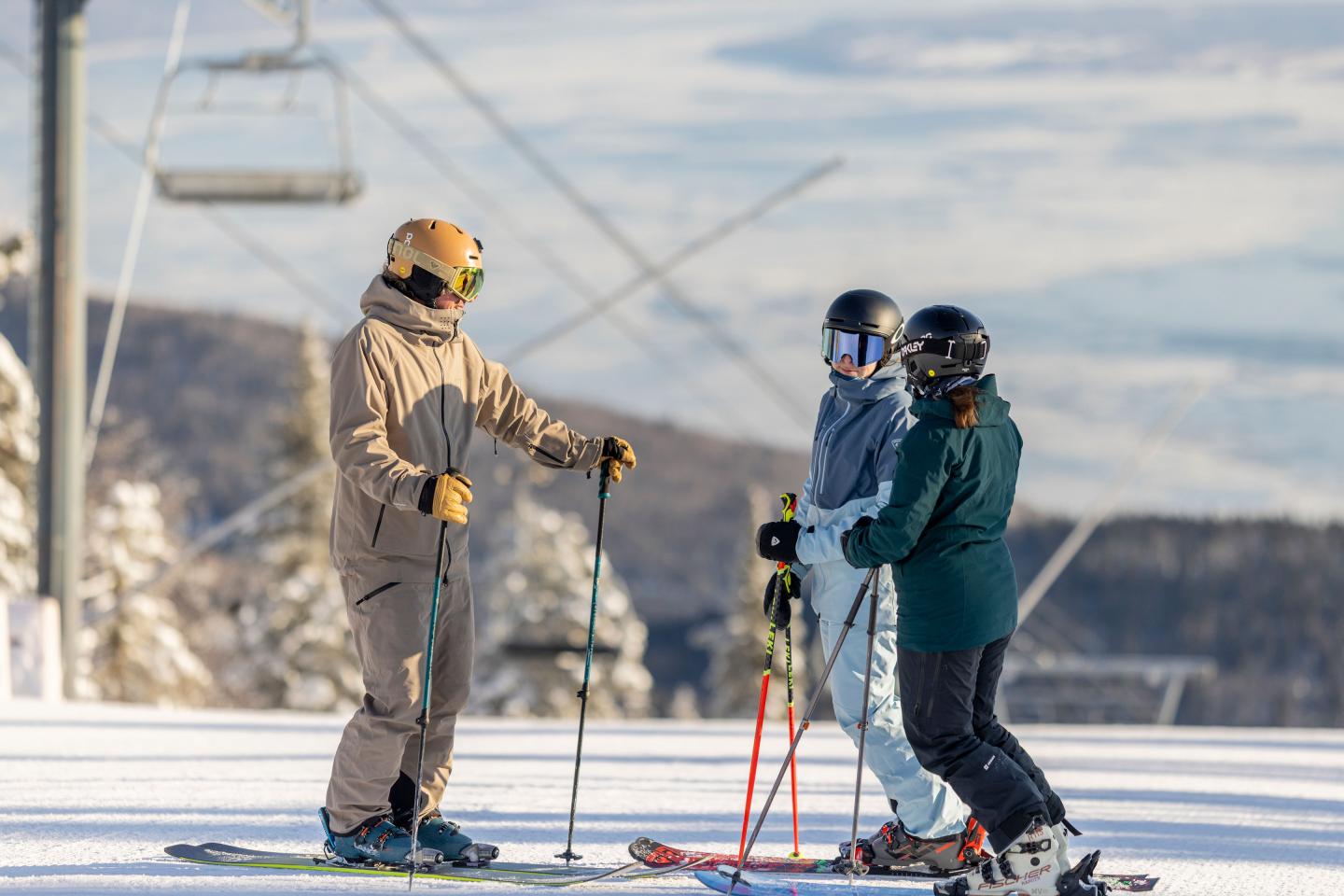 Deux skieurs discutent sur une piste enneigée, avec des remontées mécaniques en arrière-plan.