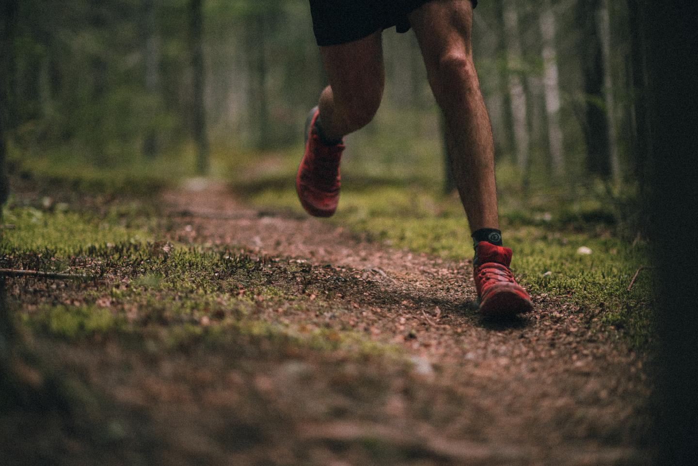 Coureur en shorts sur un sentier forestier, chaussures rouges.