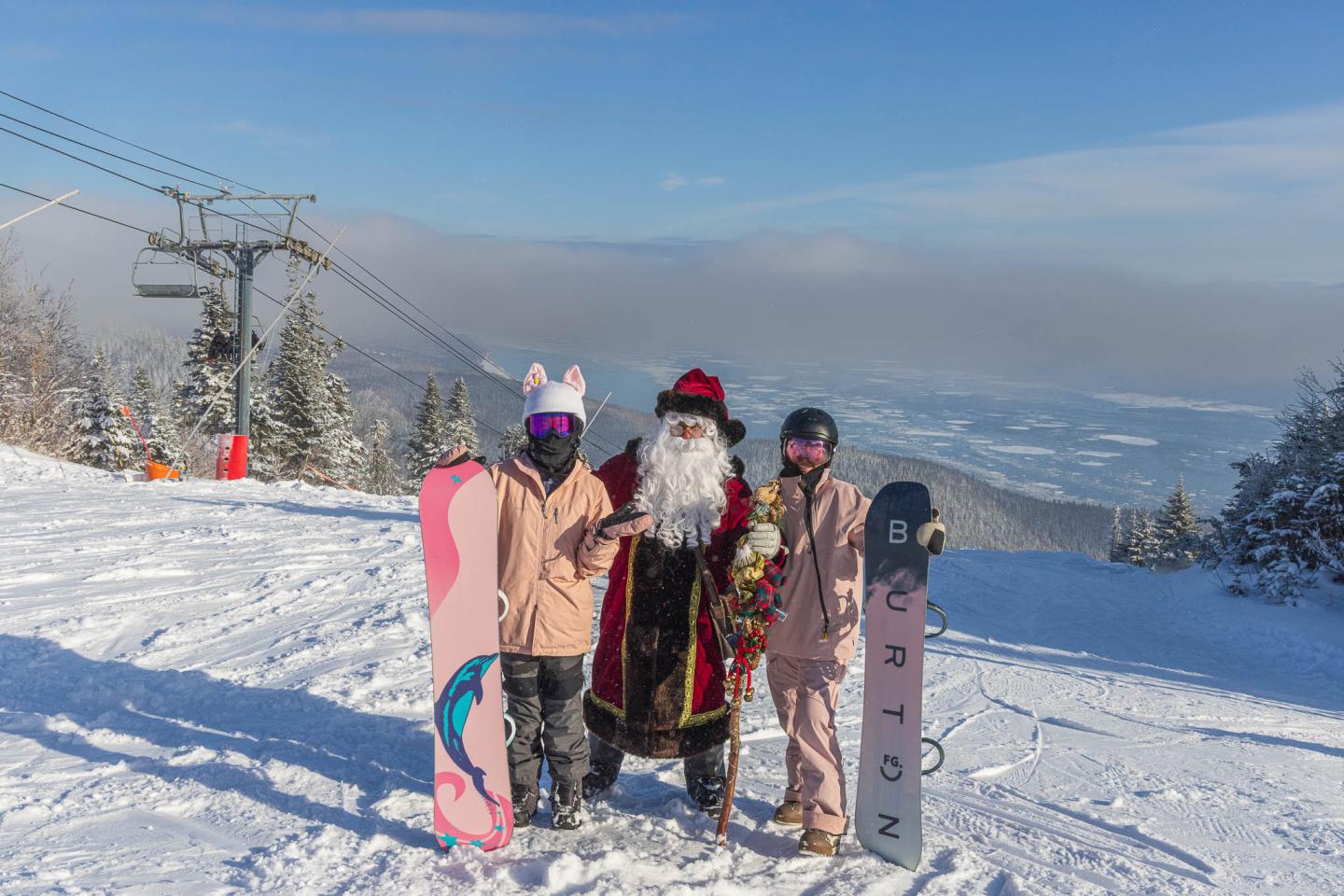 Trois enfants en tenue de ski avec snowboards sur une piste enneigée.