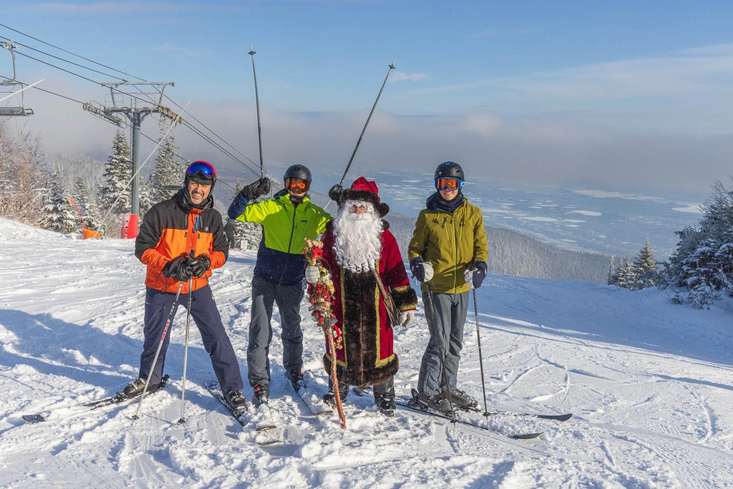 Quatre skieurs souriants sur une piste enneigée sous un ciel bleu.